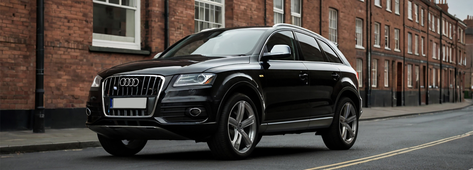 A Stylish Black Audi SUV car driving down a street next to a brick building